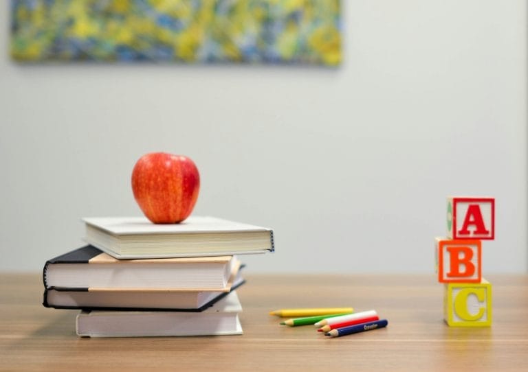 A photo of a table with books, an apple, pens, and letter blocks on it.